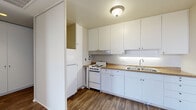 Located at 3737 Atlantic Ave in Long Beach, California, this single-floor unit offers a clean, modern aesthetic defined by neutral tones and consistent hardwood-style flooring throughout. The living area is a standout space, anchored by an expansive picture window that frames lush greenery outside, filling the room with abundant natural light and sheer curtain panels that soften the brightness. The open layout flows naturally between the living space and adjacent rooms, creating a cohesive and airy feel. The kitchen is efficiently designed with crisp white cabinetry extending from floor to ceiling, offering generous storage, complemented by a classic white range, a double basin sink, and warm-toned countertops. A tall pantry-style cabinet provides additional storage utility. The hallway features recessed lighting and built-in floor-to-ceiling closet doors, maximizing storage while maintaining a streamlined look. The bedroom benefits from its own large picture window overlooking neighborhood rooftops and the surrounding cityscape, along with a ceiling fan for added comfort. A spacious built-in closet with full-height bi-fold doors adds further practicality. Throughout the unit, the light-filled interiors, neutral palette, and wood-look flooring create a welcoming and versatile living environment.