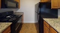 Located at 1 Lilac in Dover, New Hampshire, this single-floor unit offers a practical and well-organized layout designed for comfortable everyday living. The open living and dining area is finished with durable tile flooring and features a sliding glass door dressed with vertical blinds, allowing natural light to fill the space and providing access to the outdoors. A wall-mounted air conditioning unit ensures year-round comfort.

The kitchen is efficiently laid out with warm wood cabinetry, granite countertops, and a full suite of black appliances including a refrigerator, electric range, and over-the-range microwave. Tile flooring continues throughout this area, complementing the cabinetry tones.

The bedrooms are carpeted in a neutral, light tone, creating a cozy and quiet retreat. One bedroom features a window with views of the surrounding neighborhood, allowing for natural light and ventilation.

The bathroom is well-appointed with a vanity topped with granite countertops, warm wood cabinetry below, a large mirror, tile flooring, and a full shower-tub combo. The neutral color palette throughout the unit creates a clean, move-in-ready atmosphere that is easy to personalize.
