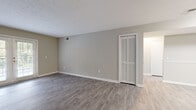 Located at 300 Carpenter Dr in Sandy Springs, GA, this single-floor unit offers a well-designed layout with a clean, modern aesthetic throughout. The open-concept living and dining area is finished with durable wood-style laminate flooring in a warm gray tone, neutral wall colors, and bright white trim that create a cohesive and welcoming atmosphere. A set of French doors at the far end of the living area allows natural light to pour in while providing a direct view to the outdoors. The kitchen is separated by a partial wall, featuring white shaker-style cabinetry, light stone countertops, and stainless steel appliances including a full-size refrigerator. The bedrooms are carpeted for comfort and include ceiling fans with lighting fixtures, standard windows with blinds, and reach-in closets with wire shelving for practical storage. The bathroom is outfitted with white cabinetry, speckled stone countertops, a single undermount sink with brushed nickel hardware, and a shower/tub combination. An additional open room with laminate flooring offers flexible use as a secondary living space or home office. The overall design is clean, functional, and move-in ready.