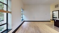 This 2-bedroom, 2-bathroom unit at 50 W Fourth St in downtown Winston-Salem offers a well-designed open-concept layout. The kitchen is a standout, featuring dark cabinetry, granite countertops, stainless steel appliances, a large island with a built-in sink, and pendant track lighting. It flows seamlessly into the dining and living areas, which are brightened by multiple windows with urban and tree-lined views. Light hardwood floors and bold dark baseboards run throughout, adding contrast. Both bedrooms include ceiling fans, natural light, and walk-in closets with wire shelving systems. The two bathrooms are finished with clean white tub-shower combos and brushed nickel fixtures.
