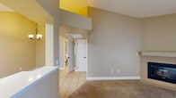 This single-floor residence offers a well-considered layout with a blend of tile and plush carpet flooring throughout. The living room is a standout space, featuring dramatic vaulted ceilings accented by a bold yellow architectural detail, a tile-surround fireplace, and a sliding glass door fitted with vertical blinds that allow for natural light and outdoor access. The open feel of the living area is enhanced by the soaring ceiling height and neutral warm-toned walls.

The galley-style kitchen is thoughtfully designed with rich dark cabinetry, white countertops, light tile flooring, and black appliances including a gas range and built-in microwave. A chandelier in the adjacent dining area adds a decorative touch to the space.

The bedrooms are carpeted and comfortably sized, each featuring arched panel doors. One bedroom includes a ceiling fan with a light fixture and a window with blinds for natural light. The bathroom features large-format tile wall surrounds encasing a soaking tub and shower combination, complemented by oil-rubbed bronze fixtures and tile flooring, giving it a clean and modern aesthetic. Throughout the home, consistent neutral tones and white trim create a cohesive and welcoming ambiance.