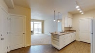 This single-floor residence offers a thoughtfully designed layout that balances functionality and comfort throughout. The open-concept kitchen flows seamlessly into the living area, anchored by a peninsula with granite-style countertops, an undermount sink, and elegant pendant lighting overhead. White cabinetry with brushed nickel hardware lines the kitchen walls, complemented by wood-look flooring and a full suite of white appliances, including a refrigerator, electric range, and built-in microwave. The spacious living room is finished with plush carpeting and transitions to a private balcony through a sliding glass door, bringing in generous natural light and outdoor views. The bedrooms are bright and generously proportioned, each featuring soft carpet, ceiling fans, and multiple windows that fill the rooms with daylight. One bedroom stands out with dual closets offering abundant storage. The bathroom is finished with a granite-style vanity countertop, white cabinetry, and a large mirror, maintaining a clean and cohesive aesthetic. Warm neutral tones and consistent finishes throughout create a welcoming and unified ambiance across the entire residence.