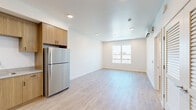 Located at 910 20th St, Unit 210 in Bakersfield, California, this thoughtfully designed unit offers a clean, modern aesthetic across a well-organized single-floor layout. Light wood-tone luxury vinyl plank flooring runs throughout the entire space, creating a cohesive and contemporary feel. The kitchen is a standout feature, equipped with warm wood cabinetry extending floor to ceiling, stainless steel appliances including a refrigerator, dishwasher, range, and over-the-range microwave, as well as light-toned countertops and a undermount sink. Recessed lighting illuminates the kitchen and living areas, which flow seamlessly together in an open-plan arrangement. A wall-mounted mini-split system provides efficient climate control. The bedroom is a comfortable retreat, benefiting from a large window that invites natural light and outdoor views of the surrounding neighborhood. A generously sized walk-in closet with wraparound shelving and hanging rods provides ample storage. The bathroom is clean and functional, featuring wood-look flooring, a soaking tub with shower, toilet, and a vanity with cabinetry. Throughout the unit, crisp white walls and bright recessed lighting contribute to an airy, well-lit ambiance. The overall design is modern, minimal, and move-in ready.