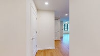 Located at 3445 Washington Blvd in Arlington, VA, this two-bedroom, two-bathroom residence offers a thoughtfully designed single-floor layout. Light hardwood flooring flows throughout the main living areas, complemented by crisp white walls and recessed lighting that create a clean, modern aesthetic. The open-concept living, dining, and kitchen area serves as the heart of the home, bathed in natural light from large, floor-to-ceiling windows that frame views of the surrounding Arlington cityscape. The kitchen is well-equipped with warm wood cabinetry extending to the ceiling for ample storage, dark countertops, and a full suite of black appliances including a gas range, refrigerator with ice maker, microwave, and dishwasher. A hallway with convenient louvered closet doors connects the main living space to the private quarters. Both bedrooms feature plush carpeting and bright white walls, with the second bedroom offering additional natural light through a large window. Three closets provide generous storage throughout. The two bathrooms are finished with neutral tile flooring; one features a full tub-shower combination with large-format tile surround and curved curtain rod, while the second offers a clean, minimalist design with a wood-toned vanity.