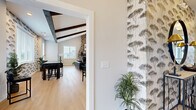 Located at 40 Red Mill Rd in Etters, PA, this single-floor community amenity space offers a thoughtfully designed layout that blends comfort, functionality, and modern style. The combined dining and living area serves as the centerpiece of the space, boasting soaring vaulted ceilings with distinctive dark-stained exposed wood beams and light hardwood flooring throughout. A dramatic floor-to-ceiling stacked stone fireplace anchors one end of the room, providing a warm and inviting focal point. An elegant gold chandelier illuminates the dining area, which is complemented by a kitchenette with dark cabinetry, open shelving, and a sliding barn door. Multiple windows flood the space with natural light and offer views of the surrounding community. A separate living room area features the same exposed beam ceiling detail, with ample seating and wall-mounted television for relaxed gatherings. The hallway connects the common areas with clean white panel doors, light wood flooring, and safety fixtures integrated seamlessly into the design. The spacious exercise room is outfitted with rubber flooring, ceiling fans, treadmills, ellipticals, weight benches, a cable machine, and a dumbbell rack, all accented by large windows and a wall-length mirror to maximize the sense of space.