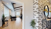 Located at 40 Red Mill Rd in Etters, PA, this single-floor community amenity space offers a thoughtfully designed layout that blends comfort, functionality, and modern style. The combined dining and living area serves as the centerpiece of the space, boasting soaring vaulted ceilings with distinctive dark-stained exposed wood beams and light hardwood flooring throughout. A dramatic floor-to-ceiling stacked stone fireplace anchors one end of the room, providing a warm and inviting focal point. An elegant gold chandelier illuminates the dining area, which is complemented by a kitchenette with dark cabinetry, open shelving, and a sliding barn door. Multiple windows flood the space with natural light and offer views of the surrounding community. A separate living room area features the same exposed beam ceiling detail, with ample seating and wall-mounted television for relaxed gatherings. The hallway connects the common areas with clean white panel doors, light wood flooring, and safety fixtures integrated seamlessly into the design. The spacious exercise room is outfitted with rubber flooring, ceiling fans, treadmills, ellipticals, weight benches, a cable machine, and a dumbbell rack, all accented by large windows and a wall-length mirror to maximize the sense of space.
