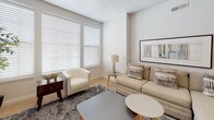 This single-floor residence offers a thoughtfully designed layout that balances open communal spaces with comfortable private quarters. The kitchen serves as a central highlight, featuring stainless steel appliances — including a full-size refrigerator, electric range, and over-the-range microwave — paired with crisp white cabinetry and dark granite-style countertops. A peninsula with a matching dark countertop extends into the living area, providing additional workspace and a natural divide between the kitchen and living spaces. Light wood-style flooring runs throughout the main areas, adding warmth to the contemporary aesthetic.

The living room benefits from large windows dressed with white horizontal blinds, allowing ample natural light to fill the space. Neutral tones and a textured ceiling contribute to a clean, understated ambiance. A hallway connects the living area to the private rooms, each carpeted in soft neutral tones and equipped with windows that invite natural light. Both bedrooms offer comfortable proportions suitable for standard furnishings.

The bathroom maintains the home's clean design language, featuring a soaking tub with an overhead shower, wood-look tile flooring, and bright white walls accented by chrome fixtures. Overall, the space presents a modern, move-in-ready environment with consistent finishes throughout.
