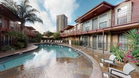 Located at 5151 Richmond Ave in Houston's vibrant Galleria district, this single-floor unit offers a thoughtfully designed layout with a clean, contemporary aesthetic throughout. The living area greets residents with warm neutral-toned walls accented by crown molding and light tile flooring, creating an inviting atmosphere. Vertical blinds allow ample natural light to filter in, brightening the space. The living room comfortably accommodates stylish furnishings and connects seamlessly to the entryway, which features a solid six-panel door and a decorative sideboard area ideal for storage and display. The kitchen is well-equipped with white cabinetry, a decorative lattice wine rack, tile countertops, a stainless steel sink, and a full suite of appliances, including a refrigerator and stove. A pass-through counter connects the kitchen to the adjacent living space, enhancing the open feel. Crown molding and recessed lighting add a refined touch to the kitchen's design. Residents also enjoy access to a beautifully landscaped outdoor pool area featuring a freeform swimming pool, a separate hot tub with natural stone surround, lounge seating beneath shade umbrellas, and lush tropical landscaping — all set against the backdrop of the Houston skyline.