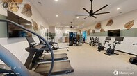 Located in Carthage, NC, this fitness center offers a spacious, thoughtfully designed exercise facility across a single floor. The interior features a cohesive aesthetic defined by a two-tone sage green and white wall treatment, complemented by decorative oversized leaf wall art that lends a natural, organic feel to the space. Light-colored carpet flooring runs throughout, while large ceiling fans and recessed lighting ensure comfort and visibility during workouts.

The cardio zone is well-appointed with TRUE-brand treadmills, stationary bikes, and additional cardio equipment, each paired with individual screens for entertainment. A dedicated strength training area includes a full dumbbell rack, weight bench, cable machines, and a multi-functional strength tower. Floor-to-ceiling mirrors along one wall visually expand the space and support form monitoring during exercise.

A functional training area is equipped with a suspension training rig, battle ropes, resistance bands, and an assortment of stability and medicine balls. Built-in wooden cubby shelving provides convenient storage for personal items. Large windows allow natural light to filter into the space, offering views to the exterior. Wall-mounted flat-screen televisions are positioned throughout for entertainment. The overall ambiance is clean, modern, and welcoming, designed to support a full range of fitness activities.