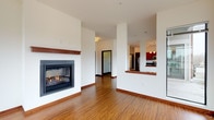 This single-floor residence presents a thoughtfully designed open-concept layout with consistent modern finishes throughout. The living area serves as the central focal point, highlighted by a sleek gas fireplace with a wood mantel set against crisp white walls. Warm hardwood-style flooring flows through the main living and kitchen areas, complemented by rich wood baseboards throughout.

The kitchen is well-equipped for everyday use, featuring rich medium-toned wood cabinetry extending to the ceiling for ample storage, dark granite countertops, and a full suite of stainless steel appliances including a range, over-the-range microwave, refrigerator, and dishwasher. A pass-through opening connects the kitchen to the living area, maintaining the open feel. Multiple windows in the kitchen bring in natural light and exterior views.

Bedrooms are finished with plush wall-to-wall carpeting and offer generous natural light. One bedroom includes access to a spacious walk-in closet with wire shelving systems providing organized storage. Two bathrooms serve the residence: one features a sliding glass-door shower enclosure, while the second includes a soaking tub/shower combo. Both bathrooms are finished with tile flooring and warm wood vanities with stone-topped counters.