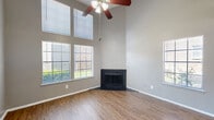 Located at 696 Fox Ave in Lewisville, TX, this two-story home offers a thoughtfully designed layout spread across two floors. The main level opens into a combined kitchen and living area, where dramatic vaulted ceilings and multiple large windows flood the space with natural light. A striking corner fireplace serves as a focal point in the living room, complemented by wood-look flooring and a ceiling fan overhead. The kitchen is well-appointed with rich dark wood cabinetry, granite countertops, a tile mosaic backsplash, black appliances, and a peninsula with a double stainless steel sink — all flowing seamlessly toward a sliding glass door that leads to the exterior. A pantry provides additional storage, and a half bathroom on this level adds convenience. The staircase, featuring a white railing, leads to the upper floor, where plush carpeting runs throughout. The upper level includes a spacious room with a vaulted ceiling, ceiling fan, and a window with natural light, along with a walk-in closet. The full bathroom on this floor offers a tiled tub-shower combination and granite-topped vanity with dark wood cabinetry, consistent with the home's cohesive design aesthetic throughout.