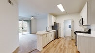Located at 1100 Dennery Rd in San Diego, CA, this single-floor residence offers a well-designed layout with modern finishes throughout. The kitchen is a standout feature, equipped with stainless steel appliances including a refrigerator, gas range, microwave, and dishwasher. Light wood-tone cabinetry pairs with marble-style countertops and a peninsula sink, creating a functional and attractive workspace that opens toward the living area. The living room is bright and airy, finished with plush carpeting, a ceiling fan, and a sliding glass door that leads to a private balcony overlooking lush greenery and a pool area, filling the space with natural light. The bedrooms are carpeted for comfort, with one featuring a spacious walk-in closet with built-in shelving. Two full bathrooms mirror each other in style, each offering a tub-shower combo, wood-look flooring, and a vanity topped with a marble-style countertop and a large mirror. A dedicated laundry area houses an in-unit washer with cabinet storage above and an electrical panel nearby. The attached garage provides convenient enclosed parking with an automatic opener. Clean white walls and consistent light wood flooring in the main areas give the home a cohesive, contemporary feel throughout.