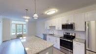 This single-floor residence at 480 Bedford Rd in Chappaqua, New York, offers a thoughtfully designed open-concept layout with modern finishes throughout. The kitchen serves as a central feature of the living space, showcasing white shaker cabinetry, granite countertops, a tile backsplash, and a full suite of stainless steel appliances including a range, microwave, dishwasher, and refrigerator. A granite-topped island with pendant lighting above provides additional prep space and casual seating, flowing seamlessly into the main living area.

The living room is bright and airy, finished with wide-plank hardwood flooring and crown molding. French doors lead to a private balcony, filling the space with natural light and outdoor views. A dedicated hallway connects the two bedrooms and bathrooms, maintaining a clear separation between living and private areas. The bedrooms feature plush carpeting, crown molding, and closets with built-in shelving. The bathrooms are finished with clean white tile, including a tub-shower combination with sliding glass doors and chrome fixtures. Throughout, the residence maintains a consistent, refined aesthetic with neutral tones and quality materials.