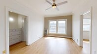 This thoughtfully designed 1-bedroom, 1-bathroom unit makes efficient use of its compact footprint across a single floor. Light hardwood flooring runs throughout the space, creating a cohesive and clean aesthetic from room to room.

The spacious bedroom occupies a generous portion of the unit and features large windows that invite abundant natural light, warm taupe accent walls, crown molding, and a ceiling fan with an integrated light fixture. A wall-mounted heating unit ensures year-round comfort, while the bright, airy atmosphere makes the room feel open and welcoming.

The galley-style kitchen is neatly organized, featuring white cabinetry that extends to the ceiling for maximum storage, a full-size refrigerator, and a gas range — all finished in white for a clean, uniform look. Recessed lighting and light hardwood flooring keep the space bright and functional.

The bathroom is well-appointed with a soaking tub and shower combination framed by soft curtains, a window allowing natural light to filter in, a modern gray vanity with open shelving and a white basin sink, and a wall-mounted mirror. The light, neutral palette gives the bathroom a fresh and serene feel.

A dedicated closet provides practical storage, and the entry area features clean white walls, light flooring, and a modern front door with keypad access. Overall, the unit offers a bright, clean, and functional living environment with consistent finishes throughout.