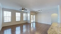 This single-story, 3-bedroom, 2-bathroom home presents a thoughtfully designed layout that balances comfort and functionality. The main living area is a standout feature, showcasing rich, dark hardwood-style flooring that runs throughout and reflects the abundant natural light streaming in from multiple windows fitted with horizontal blinds. Crown molding adds a refined architectural detail along the upper walls, lending the space a polished, finished look.

A ceiling fan centered in the living area provides both practical ventilation and a classic aesthetic touch. Track lighting near the adjacent area offers targeted illumination, enhancing versatility for various uses. A sliding glass door leads to an outdoor area, seamlessly connecting interior living with the exterior and further brightening the space with natural light.

The neutral, warm-toned walls provide a clean, move-in-ready backdrop adaptable to a variety of décor styles. The open feel of the main living space, combined with its multiple light sources—both natural and artificial—creates an inviting and airy ambiance. With three bedrooms and two full bathrooms across a single floor, this home offers convenient, accessible living without the need for stairs.