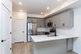Located at 1641 N 260th E in Heber City, Utah, this contemporary multi-floor home spans three levels and is designed with clean lines, neutral tones, and modern finishes throughout. The main living area features light hardwood flooring that extends through the open-concept layout, seamlessly connecting the living space to the kitchen. The kitchen is outfitted with gray shaker-style cabinetry, stainless steel appliances including a refrigerator and microwave, a peninsula with a built-in sink featuring matte black fixtures, and crisp white countertops — all illuminated by recessed lighting with a tray ceiling detail above. A bright entry area with a glass-paneled door and roller shade window allows natural light to fill the space. Bedrooms are carpeted and offer windows with views of the surrounding neighborhood. The bathrooms are finished with marble-look tile flooring, gray vanity cabinetry with matte black hardware, and white subway-tiled tub and shower surrounds. A dedicated laundry room accommodates a full-size washer and dryer. The attached garage features a panel-style door with transom windows, an automatic opener, and a concrete floor, providing ample vehicle and storage space. Throughout, the home maintains a cohesive, modern aesthetic with matte black hardware accents and a bright, neutral palette.