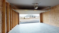 This single-story home is thoughtfully designed with functional spaces finished in a cohesive neutral palette. The attached garage is a standout feature, offering a wide double-door opening with an automatic opener installed overhead. The interior walls are partially framed with exposed OSB sheathing, and a smooth concrete floor provides a clean, durable surface. The open garage door reveals an unobstructed view of the surrounding neighborhood.

Inside, a dedicated laundry room provides practical convenience, housing a full-size GE top-load washer and dryer side by side. Wire shelving spans the width of the wall above the units, offering additional storage. Wood-look vinyl plank flooring, white trim, and a paneled interior door give the room a clean, finished appearance.

A carpeted hallway serves as the central circulation spine of the home, connecting key areas including a bathroom with visible vanity cabinetry and a living area furnished with seating. The hallway is lined with crisp white baseboards and paneled doors with brushed nickel hardware, maintaining a consistent and polished interior aesthetic throughout. Neutral wall tones and flush ceiling lighting contribute to a calm, well-organized atmosphere across the entire residence.