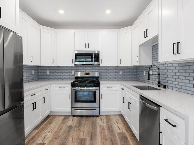 White tiled kitchen with stainless steel fridge, over, microwave, and fixtures. - Clarington Court