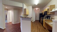 This single-floor residence offers a thoughtfully designed layout that balances functionality and comfort throughout. The open-concept living and dining area is anchored by rich, dark hardwood-style flooring, crown molding, and a ceiling fan, with natural light streaming in through multiple windows and a set of glass doors that open to the outdoors. The kitchen is positioned adjacent to the living space and features light maple cabinetry, granite-style countertops, a tile backsplash, and black appliances including a refrigerator, range, dishwasher, and microwave. A half-wall breakfast bar with a decorative shelf creates a seamless visual connection between the kitchen and the main living area. A hallway leads to the private quarters, where the bedrooms are finished with plush wall-to-wall carpeting, neutral-toned walls, and ample closet space. The bathrooms are well-appointed, each showcasing hardwood-style flooring, light maple vanity cabinetry, granite countertops, large mirrors with bright vanity lighting, and a tub-shower combination. Throughout the residence, clean white trim, panel-style doors, and a consistent warm neutral color palette contribute to a cohesive and inviting atmosphere.