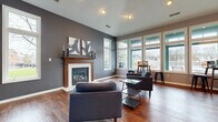 Located at 3995 Cracker Cove Ln in Canal Winchester, Ohio, this single-floor space offers a thoughtfully designed open layout that balances comfort and functionality. The main living area is anchored by a classic wood-mantled fireplace set against a bold slate-gray accent wall, complemented by rich hardwood flooring that runs throughout. Recessed lighting and vaulted ceilings enhance the sense of openness, while large, white-framed windows along multiple walls flood the interior with natural light and offer views of the surrounding neighborhood.

A dedicated workspace or flex area is positioned near a generous bank of floor-to-ceiling windows, making it an ideal spot for productivity or casual gatherings. This area accommodates both a bistro-style high table with stools and a larger work table with seating, demonstrating the versatility of the open floor plan.

The kitchen features warm cherry wood cabinetry, dark countertops, a tile backsplash, and tile flooring, providing a practical and well-equipped culinary space. A full-size refrigerator and ample counter space complete the kitchen's functional offerings.

Overall, the space presents a modern yet inviting ambiance, with a cohesive color palette of gray tones and natural wood elements tying the areas together seamlessly.