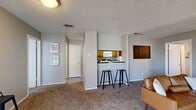 This thoughtfully designed 2-bedroom, 2-bathroom residence is laid out on a single floor, offering a comfortable and efficient use of space throughout. The open-concept living area serves as the heart of the home, featuring plush carpeting, a textured ceiling, and a wood-burning fireplace framed by multiple windows that fill the room with natural light. The adjoining kitchen is accessible via a raised breakfast bar with seating, complemented by warm wood cabinetry, dark countertops, and standard appliances. The combined dining and living area provides a seamless flow ideal for both everyday living and entertaining.

The primary bedroom is generously sized, offering carpet flooring, a ceiling fan, and a walk-in closet with built-in shelving. The second bedroom is equally inviting, also featuring carpet and a ceiling fan. Both bathrooms are finished with warm wood vanities topped with dark marble-style countertops and wood-look vinyl flooring, with one bathroom featuring a shower-tub combination. A dedicated in-unit laundry room accommodates a full-size side-by-side washer and dryer, complete with overhead shelving for added storage. Neutral gray walls and consistent finishes throughout give the residence a cohesive, modern aesthetic.