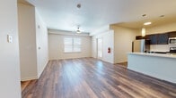 This single-floor unit offers a well-organized layout with a clear separation between living, sleeping, and utility spaces. The open-concept living and dining area is finished with wood-look plank flooring that extends throughout the main areas, complemented by neutral-toned walls and a ceiling fan overhead. Natural light enters through horizontal-blind-covered windows, and a door provides direct exterior access from the main living space.

The kitchen is positioned adjacent to the living area and features dark espresso cabinetry paired with light countertops and a full suite of stainless steel appliances, including a range, over-the-range microwave, and refrigerator. A breakfast bar with pendant lighting connects the kitchen to the open living space.

The bedrooms are carpeted and receive natural light through multiple windows. At least one bedroom includes a walk-in closet outfitted with built-in shelving and hanging rods for organized storage. The bathroom includes a glass-enclosed walk-in shower with tile surround and wood-look flooring.

A dedicated laundry area houses a full-size top-loading washer and dryer with overhead shelving, adding functional convenience to the overall layout.