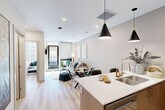 Located in downtown Edmonton, this well-appointed one-bedroom, one-bathroom unit offers a thoughtfully designed open-concept layout finished with light hardwood flooring and a neutral palette throughout. The combined kitchen and living area forms the heart of the unit, where a sleek kitchen features two-toned cabinetry in white and warm taupe, stainless steel appliances including a bottom-freezer refrigerator and gas range, a subway tile backsplash, and a peninsula with bar seating illuminated by pendant lighting. The adjoining living area provides a comfortable and bright setting, enhanced by floor-to-ceiling windows that frame urban city views and allow generous natural light to fill the space. A private balcony extends from the living area, offering direct outdoor access. The bedroom is a well-proportioned retreat featuring a large window with downtown views, recessed wall sconces, and direct access to a dedicated closet. The bathroom is finished with wood-toned tile surround, a full soaker tub with shower, a wood-front vanity with white countertop, and light hardwood-style flooring. Clean lines and modern finishes create a cohesive, contemporary ambiance throughout the entire unit.