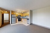 Located at 323 N 24th St in Omaha, Nebraska, this one-bedroom, one-bathroom unit offers a practical and well-organized layout across a single floor. The open-concept living and kitchen area is a central feature, with the kitchen positioned in an L-shaped configuration complete with light wood cabinetry, gray countertops, tile flooring, and a full suite of stainless steel appliances including a refrigerator, electric range, microwave, and dishwasher. Track lighting overhead ensures the kitchen is well-lit and functional. The adjacent living area features neutral-toned carpet, providing a comfortable and cohesive space. The bedroom is carpeted and receives natural light through a large window with views of surrounding greenery, creating a calm and bright atmosphere. Two interior doors in the bedroom lead to a dedicated walk-in closet fitted with wire shelving and hanging rods, offering practical storage. The bathroom includes a full tub-shower combination, a toilet, and a wood-accented vanity with a dark countertop, set on speckled tile flooring. A hallway connects the rooms efficiently, completing the thoughtful floor plan of this compact yet complete unit.