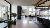 This thoughtfully designed single-floor amenity space makes a striking first impression through its grand lobby lounge, distinguished by soaring double-height ceilings and expansive steel-framed windows that flood the interior with natural light. The polished terrazzo flooring reflects the geometric pendant chandelier overhead, which cascades across the ceiling in an artful grid pattern, anchoring the space with visual drama. A central seating area is furnished with velvet lounge chairs on gold-toned bases, leather sofas, and round marble-topped tables, creating an inviting environment for gathering or relaxing. Built-in wood-paneled cabinetry frames a wall-mounted television, adding warmth against the crisp white walls.

An entry zone with a shuffleboard table and botanical-patterned wallcovering transitions seamlessly into a dedicated game room featuring a full-size billiards table, a large flat-screen TV, mirrored geometric wall art, and a plush area rug. This room is further enhanced by floor-to-ceiling windows offering panoramic outdoor views, complemented by stylish sconce lighting and patterned wallpaper. Throughout the space, lush indoor plants add a natural, organic element, while the cohesive design palette of deep blues, warm woods, and matte black accents lends the entire space a polished, contemporary character.