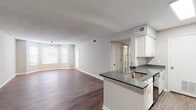 This single-story unit offers a well-designed, open-concept layout that seamlessly connects the living area and kitchen. Wood-look flooring extends throughout the space, providing a cohesive and clean aesthetic. Neutral gray and beige tones on the walls complement the bright white baseboards and trim, creating a light, airy atmosphere.

The living area is generously sized, featuring a ceiling fan with light fixture and multiple windows fitted with horizontal blinds that allow natural light to filter in. The open flow from the living space into the kitchen makes the area feel expansive and functional.

The kitchen is equipped with white cabinetry, dark gray countertops, a peninsula with an undermount sink and modern pull-down faucet, and black appliances including a refrigerator, range, and built-in microwave. Light-toned flooring in the kitchen contrasts subtly with the darker wood-look floors in the living areas.

The bedrooms each feature ceiling fans, natural light from windows, and access to closet space. Two bathrooms serve the unit, both finished with white vanity cabinetry, dark countertops, and wood-look flooring. The textured walls in the bathrooms add a distinctive design element, and each includes a tub-shower combination. A textured ceiling is consistent throughout the unit.