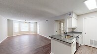 This single-story unit offers a well-designed, open-concept layout that seamlessly connects the living area and kitchen. Wood-look flooring extends throughout the space, providing a cohesive and clean aesthetic. Neutral gray and beige tones on the walls complement the bright white baseboards and trim, creating a light, airy atmosphere.

The living area is generously sized, featuring a ceiling fan with light fixture and multiple windows fitted with horizontal blinds that allow natural light to filter in. The open flow from the living space into the kitchen makes the area feel expansive and functional.

The kitchen is equipped with white cabinetry, dark gray countertops, a peninsula with an undermount sink and modern pull-down faucet, and black appliances including a refrigerator, range, and built-in microwave. Light-toned flooring in the kitchen contrasts subtly with the darker wood-look floors in the living areas.

The bedrooms each feature ceiling fans, natural light from windows, and access to closet space. Two bathrooms serve the unit, both finished with white vanity cabinetry, dark countertops, and wood-look flooring. The textured walls in the bathrooms add a distinctive design element, and each includes a tub-shower combination. A textured ceiling is consistent throughout the unit.