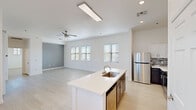 This single-story unit offers a well-designed open-concept layout that maximizes its generous footprint. The combined kitchen and living area serves as the heart of the space, characterized by light wood-style flooring, recessed lighting, and a large flush ceiling light fixture. A ceiling fan adds functionality to the living area, which receives natural light through multiple windows fitted with horizontal blinds. A sliding glass door with vertical blinds provides access to an outdoor area.

The kitchen is thoughtfully equipped with stainless steel appliances, including a refrigerator, range, and microwave. White upper cabinetry contrasts with dark lower cabinets, complemented by a mosaic tile backsplash and white quartz countertops. A central island features an undermount sink and additional storage beneath.

The spacious bedroom accommodates a ceiling fan, multiple windows with outdoor views, and direct access to a generously sized walk-in closet outfitted with double hanging rods and built-in shelving. The bathroom features a sliding glass-enclosed walk-in shower with tile accents and a window for natural light. Light-toned flooring flows consistently throughout the entire unit, reinforcing its clean, modern aesthetic.