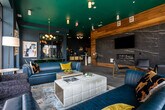 Located at 1399 Delashmut Ave in Columbus, Ohio, this contemporary residential lobby is a thoughtfully designed communal space that makes a striking first impression. The single-floor layout is defined by its bold, signature teal ceilings that contrast dramatically with deep navy blue walls, creating a vivid and cohesive design identity throughout.

The entrance area features elegant herringbone-patterned wood flooring, a warm wood-clad accent wall, and tufted white lounge chairs that provide a welcoming seating vignette. A reception desk greets visitors upon entry, while decorative wall sconces, circular mirrors, and curated artwork add character and depth.

The expansive lounge area is bathed in natural light from floor-to-ceiling windows that wrap around the space, offering open views of the Columbus skyline and surrounding neighborhood. Multiple seating arrangements — including plush blue sofas, armchairs, and accent chairs — furnish the area for both social gatherings and quiet relaxation.

A dining area with a sleek dark table and emerald green chairs sits beneath a sculptural globe chandelier, adjacent to glass-paneled office partitions. A marble-surround linear fireplace with an integrated TV serves as a refined focal point, flanked by warm wood paneling and high-top bistro seating. The overall ambiance is modern, curated, and inviting.