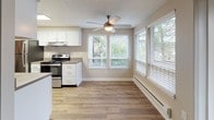 This single-floor residential unit offers a thoughtfully designed layout that balances functionality and comfort throughout. The galley-style kitchen is a standout feature, outfitted with white shaker cabinetry, taupe laminate countertops, wood-look vinyl flooring, stainless steel appliances including a range and refrigerator, and a skylight-style overhead fixture that keeps the space bright and practical.

Adjacent to the kitchen, the dining area benefits from large windows with horizontal blinds that invite natural light and views of surrounding greenery, complemented by a ceiling fan overhead. The open living area flows seamlessly from the dining space, featuring dark hardwood-style flooring, neutral gray walls, a textured ceiling, and baseboard heating.

The bedrooms are carpeted for warmth and comfort, each with neutral tones, textured ceilings, and windows providing natural light. One bedroom includes a built-in closet with double doors and dedicated shelving. The unit includes two bathrooms: a full bathroom with a soaking tub, overhead shower, wood-look flooring, and a vanity with taupe countertops; and a half or secondary bathroom with matching finishes and a single-basin vanity. Clean white trim and brushed nickel hardware lend a cohesive, modern feel throughout the space.