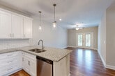 Located at 1220 Pleasant Ridge Rd in Greensboro, NC, this single-floor, 2-bedroom, 2-bathroom residence offers a thoughtfully designed layout with modern finishes throughout. The open-concept kitchen and living area serves as the heart of the home, anchored by a central island with granite countertops, a double sink, and a stainless steel dishwasher. White shaker cabinetry, a classic subway tile backsplash, and a full suite of stainless steel appliances — including a refrigerator, range, and microwave — complete the kitchen. Pendant lighting over the island and a ceiling fan in the living area add both style and function, while French doors at the far end of the living room invite natural light and provide access to an outdoor space. Rich hardwood flooring flows throughout the main living areas, transitioning to plush carpet in both bedrooms. The spacious primary bedroom includes a ceiling fan and ample closet space with double doors. The second bedroom is equally comfortable with its own ceiling fan and closet access. Both bathrooms feature granite-topped vanities and hardwood flooring, with a tub-shower combination in one bath. A dedicated laundry area with a full-size washer and overhead shelving adds everyday convenience to this well-rounded home.