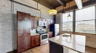 This single-floor unit at 206 Cesar E Chavez Ave SW blends industrial character with modern finishes throughout. The kitchen serves as a central focal point, showcasing rich dark wood cabinetry, granite countertops, and a large island with an undermount sink and dishwasher. Stainless steel appliances, including an electric range with microwave and a full-size refrigerator, complete the well-appointed space. Exposed ductwork and pendant lighting hang from elevated ceilings, contributing to the space's industrial aesthetic.

Painted white brick walls appear throughout the unit, lending texture and historic character to each room. Wide-plank hardwood flooring runs through the kitchen and living areas, while carpeting covers the bedroom spaces. The bedrooms feature high ceilings with exposed mechanical systems overhead, closet access, and connections to adjacent rooms. Windows throughout the unit admit natural light and offer urban views of the surrounding Grand Rapids neighborhood.

The bathroom continues the industrial theme with painted brick walls, tile flooring, a soaking tub, and a granite-topped vanity with an industrial-style sconce. Overall, the space offers a compelling mix of raw architectural detail and contemporary upgrades.