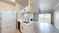 Located in Plano, TX, this one-bedroom, one-bathroom residence offers a well-designed single-floor layout that makes efficient use of its space. The open-concept kitchen and living area serves as the heart of the unit, where light wood-style flooring flows throughout, complemented by crown molding and a ceiling fan. The kitchen features white cabinetry with black hardware, light countertops, a peninsula with a single-basin sink and a sleek black pull-down faucet, and black appliances including a range, microwave, refrigerator, and dishwasher. A classic tile backsplash adds a clean, polished finish. The living room is anchored by a fireplace flanked by built-in shelving and opens to the outdoors through a sliding glass door, allowing natural light to fill the space. The bedroom is a comfortable retreat with a large window, ceiling fan, and direct access to a generously sized walk-in closet outfitted with multi-tier wire shelving for ample storage. The bathroom includes a full soaking tub and shower combination with white tile surround. A dedicated laundry area completes this thoughtfully arranged home, offering practical convenience within a clean, neutral aesthetic throughout.