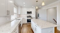 Located at 1 Kowal St, Unit I5 in Clifton, NJ, this well-appointed 2-bedroom, 1-bathroom unit offers a thoughtfully designed layout with attractive finishes throughout. The standout feature is the beautifully renovated kitchen, which boasts crisp white shaker cabinetry, a large center island topped with stone countertops, stainless steel appliances including a gas range, built-in microwave, dishwasher, and refrigerator, plus pendant lighting and recessed lights that brighten the space. Hardwood floors flow throughout the main living areas and bedrooms, lending warmth and continuity. Both bedrooms are comfortably proportioned, dressed in neutral tones with crown molding, ceiling fans, and windows that bring in natural light. The full bathroom features tile flooring, a tub-shower combination with mosaic tile accent, a white vanity with undermount sink, and a bright window. A hallway connects the key living spaces, while three closets provide generous storage options. The unit also includes a dedicated laundry area for added convenience. A staircase with rich wood treads and white risers, complemented by a warm wood handrail, adds a classic touch to the interior. Clean lines, neutral palettes, and quality finishes make this a move-in ready home.