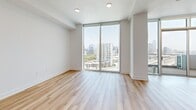 Located in Dallas's vibrant Design District at 1400 Hi Line Drive, this contemporary single-floor residence offers a thoughtfully designed open layout bathed in natural light. Light-toned hardwood flooring flows throughout, complementing the clean, modern aesthetic of the white walls and crisp trim.

The open-concept kitchen and living area serves as the heart of the unit. The kitchen is outfitted with white shaker cabinetry accented by gold hardware, stone countertops, stainless steel appliances, a central island with pendant lighting, and a built-in barn door that adds a stylish architectural touch. Floor-to-ceiling glass walls flood the living area with abundant natural light and provide direct access to a spacious private balcony, where panoramic views of the Dallas skyline and surrounding cityscape create a dramatic backdrop.

A dedicated living room offers additional space and features a ceiling fan and access to the expansive windows that frame city views. The bathroom is well-appointed with a stone-topped vanity, tile flooring, and a glass-enclosed shower. A separate laundry room provides in-unit washer and dryer hookups alongside generous built-in shelving. A connecting hallway ties the spaces together, ensuring a functional and cohesive flow throughout this sleek urban residence.