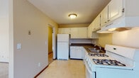 This single-floor unit offers a practical and comfortable layout designed for everyday living. The kitchen is efficiently arranged with white cabinetry providing ample storage, dark countertops, a double-basin sink, a gas range, and a full-size refrigerator, all set on light tile flooring. A range hood and textured ceiling complete the utilitarian yet tidy space.

The living area is generously proportioned, featuring wall-to-wall carpet, warm beige tones, and a large sliding glass door that invites abundant natural light and provides outdoor views. Baseboard heating runs along the exterior walls, ensuring comfort throughout the seasons.

The bedrooms are carpeted and bright, each equipped with a ceiling fan and wide windows framed in rich wood tones that overlook a natural, tree-lined setting. A wall-mounted air conditioning unit is present in one of the bedrooms for added climate control.

The bathrooms are clean and functional. One features a single-basin vanity with white cabinetry, a framed mirror, and tile backsplash, while the other includes a full tub-shower combination with classic white square tile surround. Both bathrooms maintain a cohesive, neutral palette that adds to the overall sense of tidiness and ease throughout the unit.