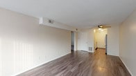 This single-floor residence offers a practical and well-organized layout across its living spaces. The main living area is generously proportioned, featuring wood-look plank flooring, neutral beige walls, and a textured ceiling. A ceiling fan provides overhead ventilation, while HVAC vents are integrated throughout. A sliding glass door at one end of the living area allows natural light to filter in, contributing to an open, airy atmosphere.

The kitchen is efficiently designed with white cabinetry, light granite-style countertops, and stainless steel appliances including an electric range and an over-the-range microwave. The flooring continues the wood-look plank theme, maintaining visual consistency with the main living space.

The bedroom is a comfortable, well-lit room with plush carpet flooring and multiple windows fitted with horizontal blinds, allowing natural light from multiple directions. The neutral color palette carries throughout, giving the room a calm and functional character.

The bathroom features a full soaking tub and shower combination with floor-to-ceiling large-format earth-toned tile surround, paired with wood-look flooring and clean white fixtures. The overall design of the unit is straightforward and functional, with consistent finishes throughout.