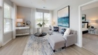 Located at 115 Great Lawn Dr in Summerville, SC, this single-story home offers a thoughtfully designed layout with modern finishes and a cohesive aesthetic throughout. Light wood-look flooring flows through the main living areas, complemented by neutral gray walls and crisp white trim.

The open-concept kitchen is a standout feature, anchored by a central island with granite countertops and bar seating for casual dining. Dark espresso cabinetry extends floor to ceiling, providing ample storage, while stainless steel appliances — including a refrigerator, microwave, and range — add a polished, contemporary touch. Pendant lighting above the island and patterned window valances lend character to the space. The kitchen opens seamlessly into a bright living area filled with natural light from multiple large windows dressed with sheer curtains.

The bedroom features plush carpeting, generous natural light, and a calm, restful ambiance. Two full bathrooms mirror each other in design, each appointed with dark espresso vanities, granite countertops, and tub-shower combinations with tile surrounds.

A welcoming entryway hallway with light-filled sight lines connects the home's spaces with ease. The dedicated laundry room offers full-size washer and dryer units with overhead shelving. Every detail of this home reflects a clean, modern sensibility suited for comfortable everyday living.