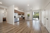 Located at 2408 S Broadway Ave in Boise, Idaho, this thoughtfully designed two-bedroom, two-bathroom residence offers a clean, modern aesthetic across a single floor. The open-concept living, dining, and kitchen area forms the heart of the home, bathed in natural light from large windows and a sliding glass door that leads to an outdoor balcony with pleasant neighborhood views. The kitchen is outfitted with warm wood-toned cabinetry, stainless steel appliances including a refrigerator with ice maker, dishwasher, microwave, and range, as well as light quartz-style countertops and a sleek black-hardware sink. Light wood plank flooring flows throughout the main living areas, complementing the bright white walls and recessed lighting overhead. The primary bedroom is generously proportioned, featuring a double-door closet, additional storage access, and light wood flooring. Its en-suite bathroom includes wood-toned cabinetry, a walk-in closet, and light wood flooring. The second bedroom features plush carpet, a window with outdoor views, and direct access to a closet. Additional highlights include an in-unit laundry area, three closets for ample storage, a hallway connecting all rooms, and a striking dark-hued entry door that adds a bold design contrast to the otherwise light and airy interior.