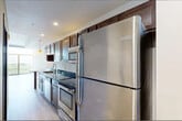 This single-floor unit offers an efficiently organized layout that maximizes its available square footage. The open-concept kitchen and living area forms the heart of the space, with light wood-tone flooring running throughout, creating a cohesive and airy atmosphere. The kitchen is well-equipped, featuring rich dark-stained wood cabinetry, dark granite countertops with a double stainless steel sink, and a full suite of stainless steel appliances including a refrigerator, electric range, built-in microwave, and dishwasher. Pendant lighting adds a warm accent above the kitchen corridor.

The living area is bright and open, benefiting from large floor-to-ceiling sliding glass doors that invite abundant natural light and provide elevated outdoor views of the surrounding cityscape. A wall sconce adds subtle ambient lighting to complement the natural light.

The bathroom continues the unit's cohesive design with dark granite countertops, a dark wood vanity with matching hardware, and neutral tile flooring. Conveniently adjacent to the bathroom is a dedicated laundry area housing a full-sized washer and dryer. A closet provides additional storage. The overall aesthetic is modern and clean, with consistent finishes tying the space together.