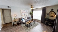 This single-story residence offers a thoughtfully arranged layout with distinct living, dining, kitchen, bedroom, and bathroom areas. The living room serves as the focal point of the home, featuring wood-look flooring, a ceiling fan, and large windows dressed with dark curtain panels that allow abundant natural light to fill the space. The room comfortably accommodates a full seating arrangement, and its neutral wall tones create a versatile backdrop.

Adjacent to the living area, the dining space is defined by a pendant light overhead and direct access to the kitchen. A breakfast bar connects the two areas, adding casual seating options. The kitchen is efficiently designed with white cabinetry, light quartz-style countertops, and stainless steel appliances including a refrigerator, electric range, and built-in microwave, all set on wood-look flooring.

The bedroom provides a comfortable retreat with plush carpet, a ceiling fan, a window for natural light, and an open walk-in closet offering practical storage. The bathroom features a single vanity with a round basin sink, light countertops, white cabinetry, and a well-lit mirror. Textured ceilings are consistent throughout the unit, contributing to its classic character.