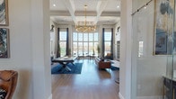 This single-floor clubhouse is designed to serve as a sophisticated social and work hub, combining elegant architectural details with versatile, well-appointed spaces. The centerpiece of the facility is a grand main lounge defined by dramatically tall ceilings, light hardwood flooring, and a sweeping floor-to-ceiling bay window wall that frames direct views of the outdoor pool area. A large-scale gold ring chandelier anchors the room, complementing the coffered ceiling detail above. A billiards table sits atop a deep blue area rug, while leather seating and bistro-style marble-top tables are arranged to encourage both casual gathering and relaxed conversation.

One corner of the lounge features a stacked-stone accent wall housing a fireplace with a mounted television above, flanked by built-in bench seating upholstered in navy blue with leather and patterned throw pillows. Sculptural wall art and framed pieces add visual interest throughout.

A private consultation or meeting nook accommodates a cluster of cognac leather wingback chairs around a central coffee table, with a wall-mounted display and a dark wood credenza providing functional storage.

The co-working area offers a long dark wood communal desk with built-in power outlets, gold accent seating, artistic pendant lighting, and wall-mounted screens—ideal for productivity in a polished environment.