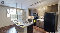 Located at 500 S Lasalle St in Durham, NC, this one-bedroom, one-bathroom residence offers a thoughtfully designed single-floor layout with a comfortable and functional living environment. The kitchen serves as a standout feature, showcasing dark wood cabinetry, granite countertops, a tile backsplash, and a generously sized island with a double stainless steel sink and pendant lighting overhead. Black appliances, including a refrigerator, range, and built-in microwave, complete the well-equipped cooking space. Rich hardwood flooring extends through the main living areas, complemented by crown molding and elegant arched doorways that lend architectural character throughout. The living area features a tray ceiling with crown molding detail and an arched window that allows natural light to fill the room. The spacious primary bedroom is finished with plush carpeting, a ceiling fan, and an arched window offering outdoor views. Two closets provide ample storage. The bathroom includes a tiled tub-shower combination set within an arched alcove, paired with granite countertops and tile flooring. Track lighting and recessed fixtures ensure well-lit spaces throughout this refined Durham residence.