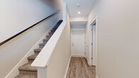 This three-story property is designed to maximize living capacity while maintaining a clean, modern aesthetic throughout. The ground floor serves as a compact entry level, featuring a welcoming hallway with wood-look flooring and carpeted staircases connecting all three floors, each equipped with sturdy railings for safety and convenience.

The main living floor hosts a generously sized open-plan kitchen and living room. The kitchen is outfitted with white shaker cabinetry, stainless steel appliances including a French door refrigerator and range, a subway tile backsplash, and a large quartz island with an undermount sink. The adjoining living area features wood-look flooring, recessed lighting, a ceiling fan, and natural light from windows overlooking the exterior.

The upper floors accommodate the seven bedrooms, including a primary suite with a dedicated walk-in closet fitted with multi-tiered shelving and hanging rods. Bedrooms feature wood-look flooring, ceiling fans, and windows providing natural light. The four bathrooms are finished consistently with white vanity cabinetry, gray countertops, wood-look flooring, and tub-shower combinations. The overall palette of soft gray walls, white trim, and warm wood-tone floors creates a cohesive, neutral ambiance throughout.