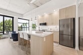 Located at 2946 Dundas St W in Toronto's vibrant Junction neighbourhood, this one-bedroom, one-bathroom unit offers a thoughtfully designed open-concept layout with modern industrial character. The exposed concrete ceiling adds an authentic loft aesthetic, complemented by light hardwood flooring and crisp white walls throughout.

The kitchen and living area flow seamlessly together, anchored by a central island with bar seating and pendant lighting. The kitchen features light wood cabinetry extending to the ceiling, white subway tile backsplash, stainless steel appliances, and ample storage. Large floor-to-ceiling windows and a sliding glass door flood the living area with natural light and frame views of the treetop canopy, while providing direct access to a private outdoor balcony equipped with seating — ideal for al fresco dining.

The bedroom is a calm, well-proportioned retreat with light flooring, a built-in sliding door closet, and soft neutral tones. The bathroom is clean and functional, finished in warm cream tiling with a full soaker tub and shower combination. The unit's overall layout maximizes the use of its footprint, delivering a comfortable and efficient living space with refined, contemporary finishes throughout.