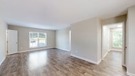 This thoughtfully designed one-bedroom, one-bathroom residence offers a clean, modern aesthetic across a single level. The open living room is a standout feature, showcasing warm hardwood-style plank flooring, neutral beige walls, and crisp white baseboards. A large window floods the space with abundant natural light and provides views of the surrounding greenery, enhancing the bright and airy atmosphere throughout.

The kitchen is efficiently laid out and well-appointed, featuring white cabinetry, granite-look countertops with subtle veining, a classic white subway tile backsplash, and stainless steel appliances including a gas range and over-the-range microwave. A window above the counter brings in natural light, making the space feel open and inviting.

The bedroom offers a comfortable, carpeted retreat with two windows that allow natural light from multiple angles. A dedicated closet with double doors provides practical storage. The neutral carpet and soft wall tones create a calm and restful environment.

The bathroom is clean and functional, featuring wood-look tile flooring, a white vanity with granite-style countertop, and a tub-shower combination. A hallway connects all rooms, contributing to an efficient and logical flow throughout this well-maintained single-floor residence.